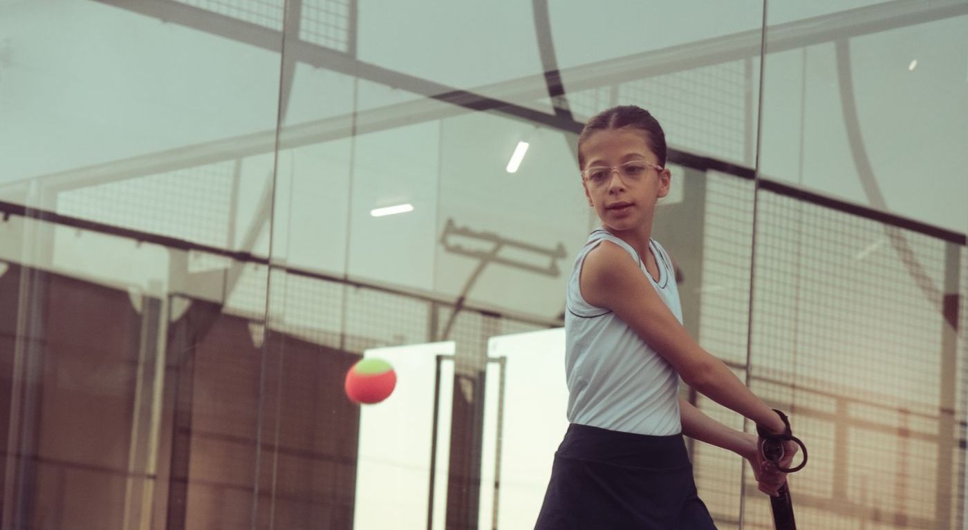 Young girl hitting a padel ball with a junior racket on an indoor court