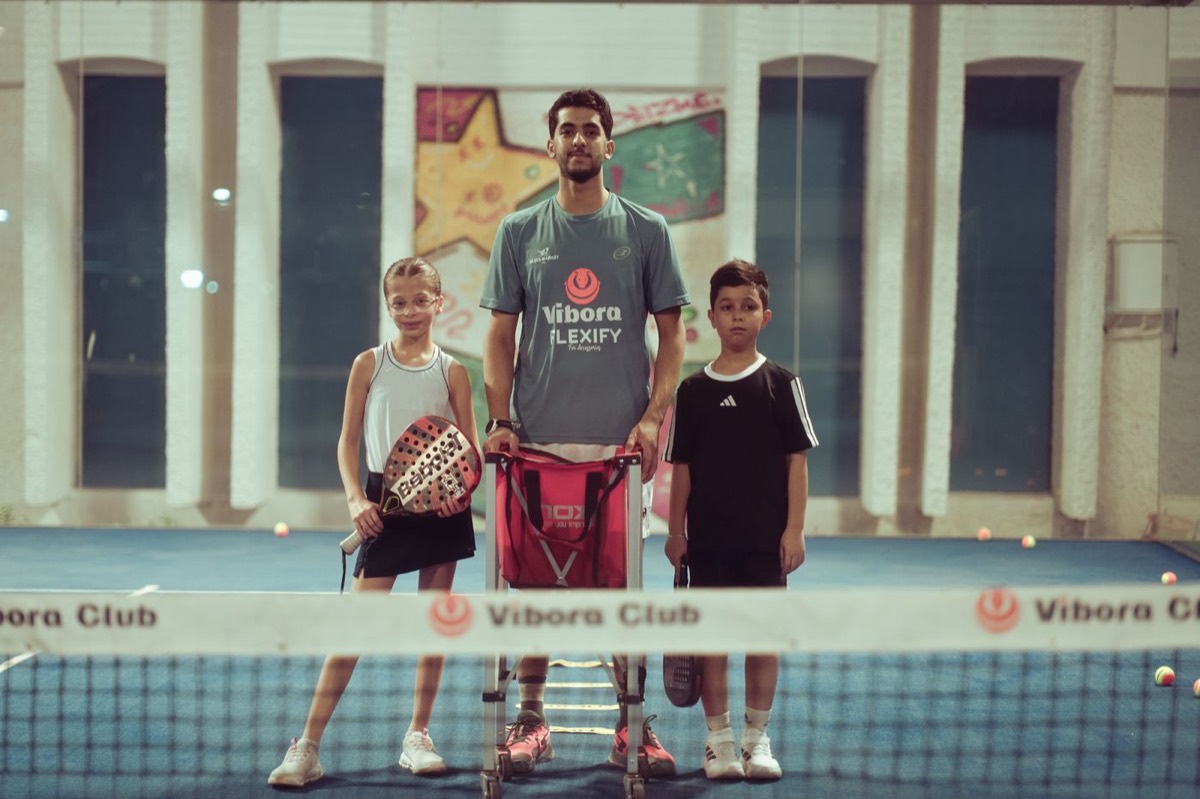 Padel coach standing with two young players at an indoor club