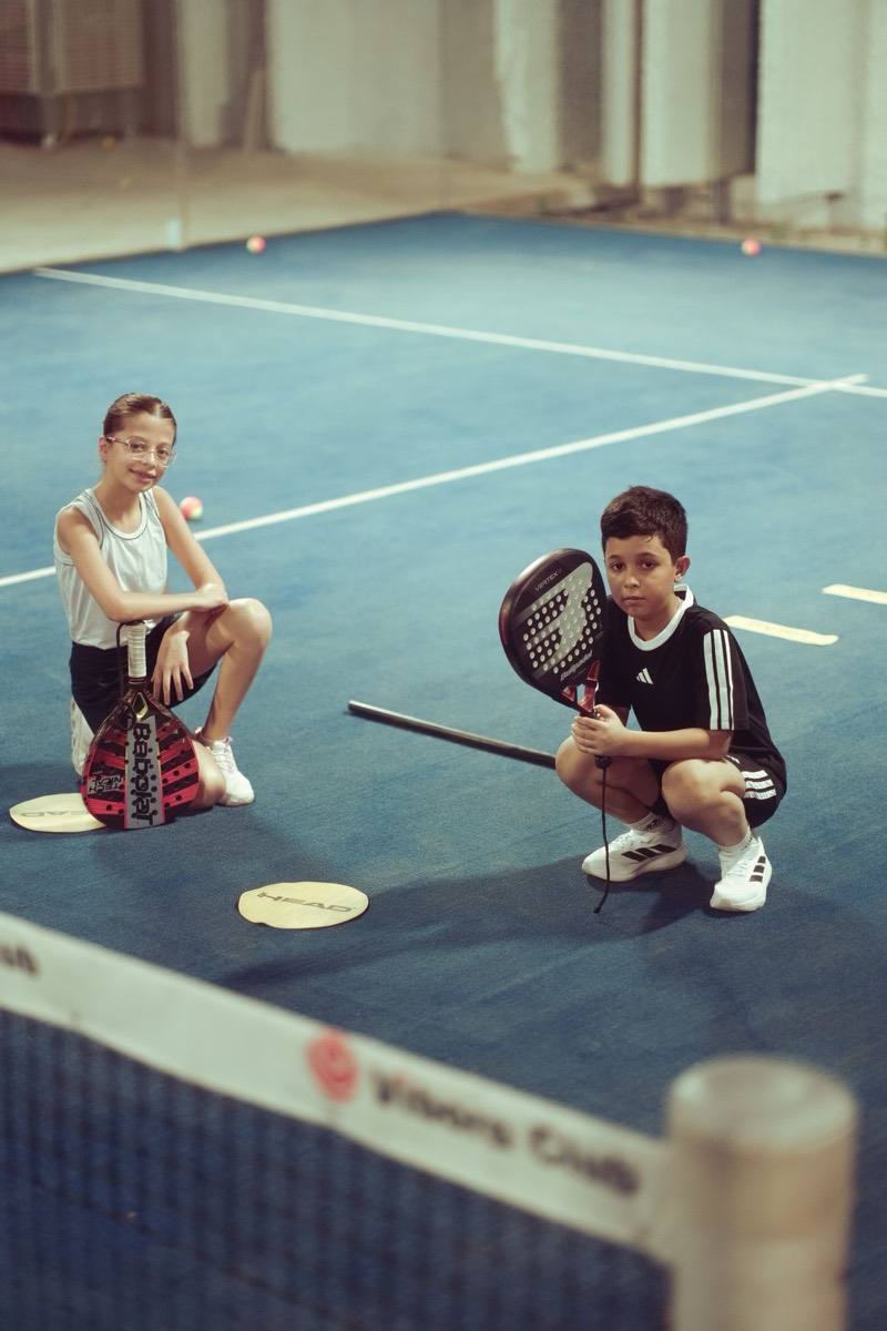 Two kids with padel rackets on an indoor court